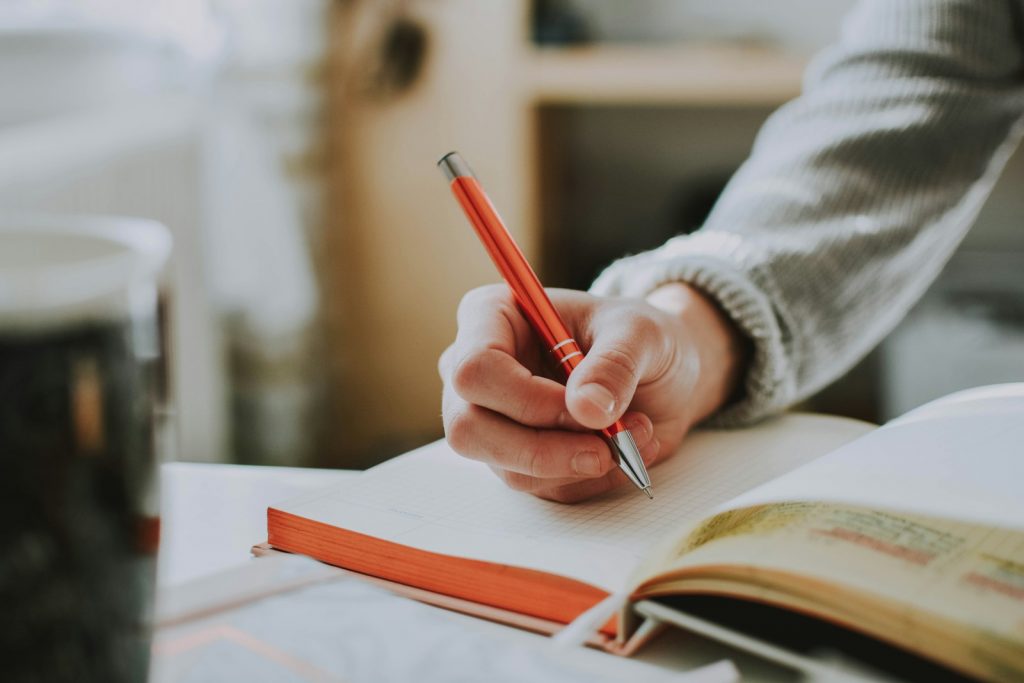 Person schreibt handschriftlich in ein Notizbuch, Symbolbild für kreatives Schreiben