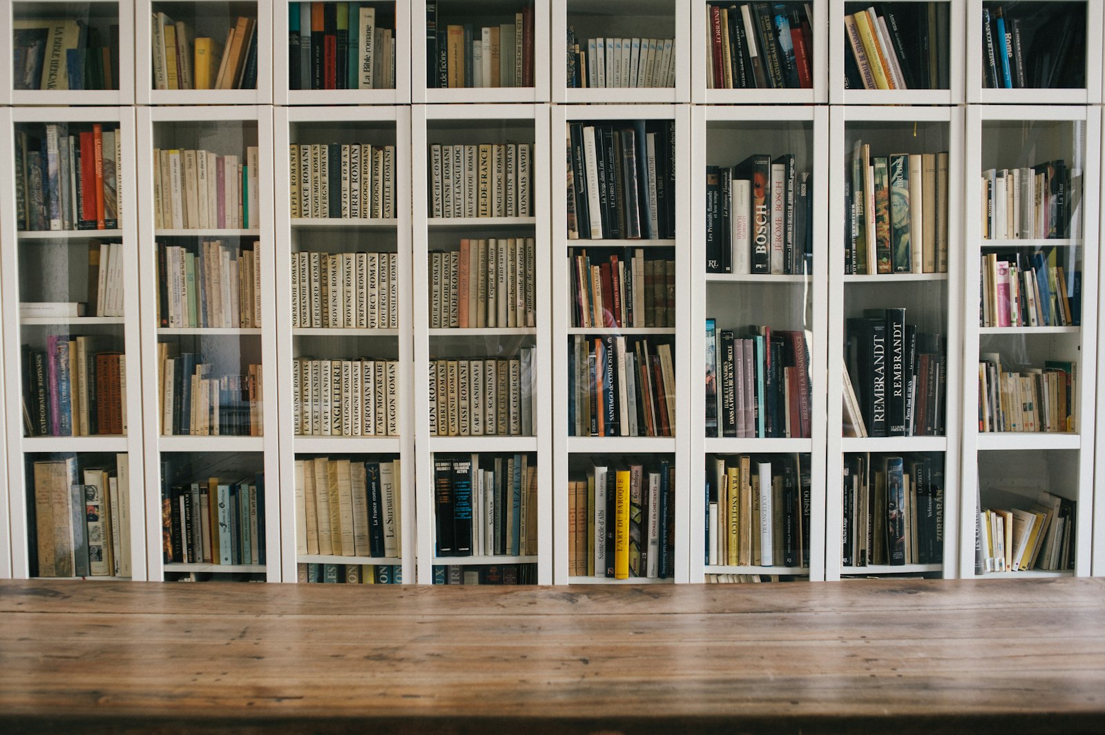 Bücher in einem weißen Regal hinter einer leeren Holztischfläche