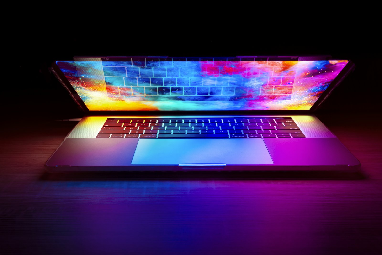 Aufgeklappter Laptop mit farbig beleuchtetem Bildschirm auf einem dunklen Tisch