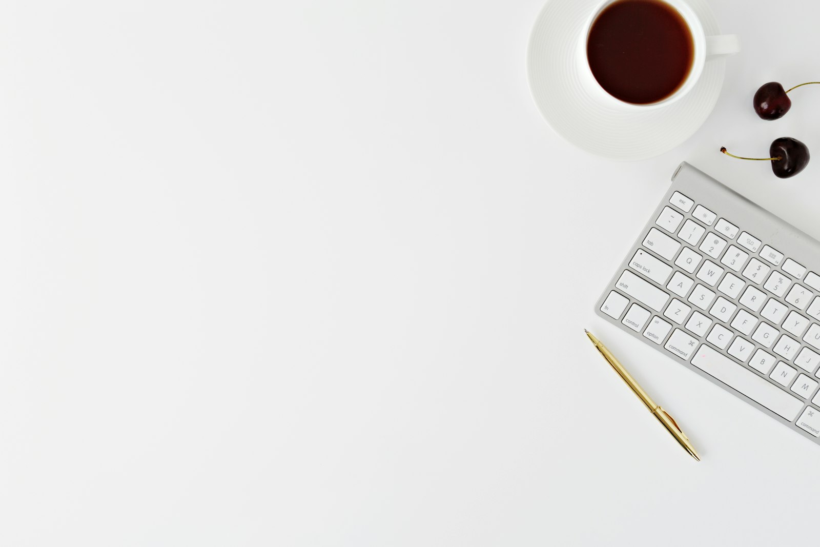 Weiße Tastatur, goldfarbener Stift und Tasse auf einem hellen Tisch