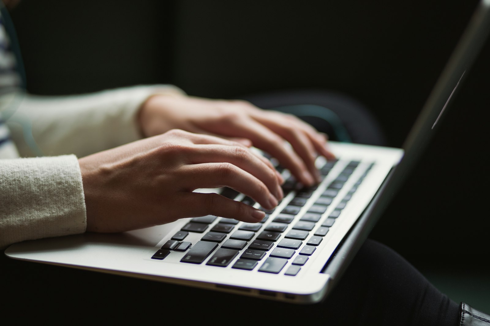 Hände tippen auf einer Laptop-Tastatur, im Hintergrund ein Online-Formular auf dem Bildschirm