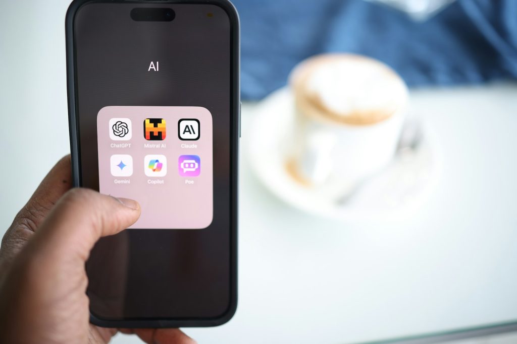 Hand hält ein Smartphone mit einem App-Ordner voller KI-Assistenten, darunter Gemini