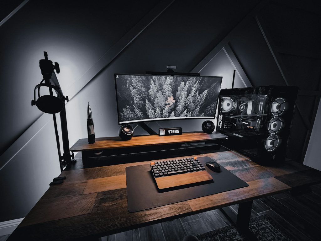 Schreibtisch mit breitem Monitor, Tastatur und geöffnetem Blick auf einen beleuchteten Desktop-PC