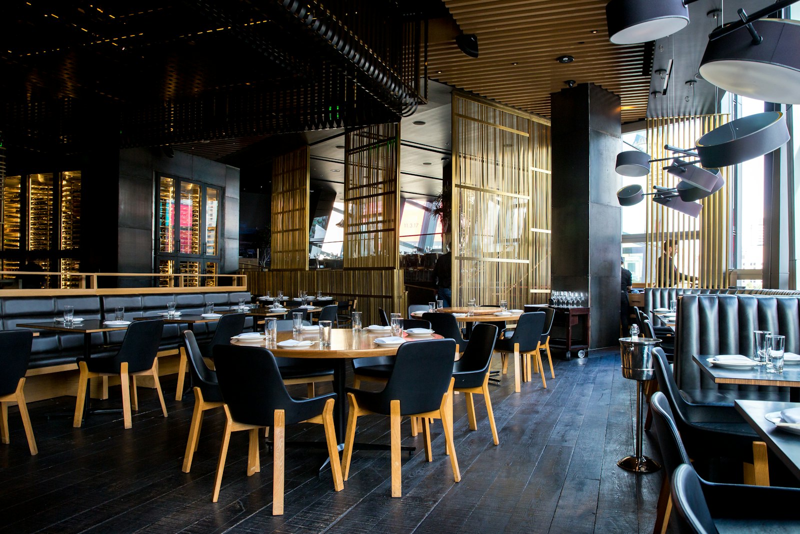Restaurant mit gedeckten Holztischen, dunklen Stühlen und großen Fenstern